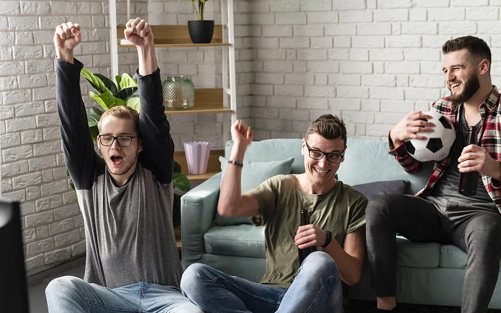 cheerful_male_friends_watching_sports_tv_with_football_beer_copy.webp